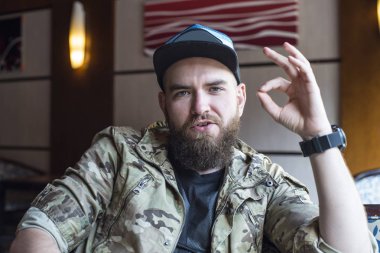 Sakallı bir adam. Adam ok gösterir. 