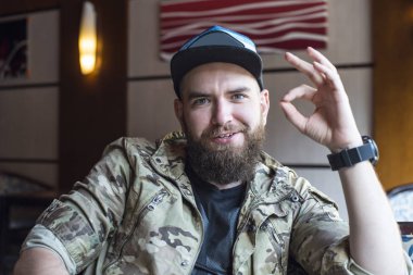 Sakallı bir adam. Adam ok gösterir. 