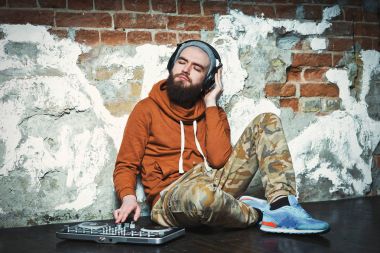 Sakallı Dj. Şapka ve spor ayakkabı giyen.