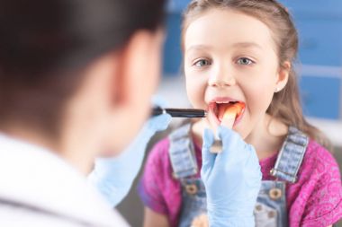 Doctor checking throat of girl clipart