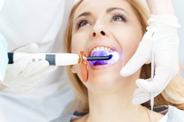Diş hekiminde hastanın dişlerini beyazlatıyor.