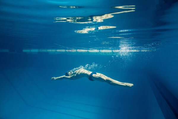 underwater picture of young swimmer in goggles exercising in swimming pool