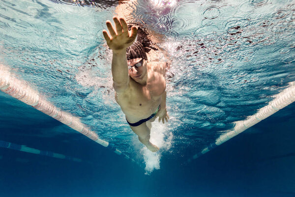 подводная фотография молодого пловца в очках, тренирующегося в бассейне
