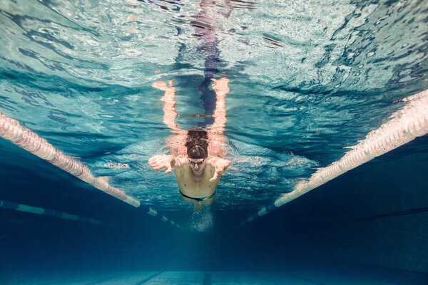 underwater picture of young swimmer in cap and goggles training in swimming pool