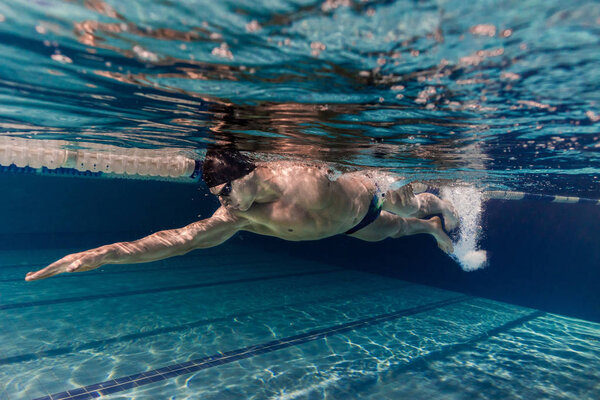 underwater picture of young swimmer in cap and goggles training in swimming pool