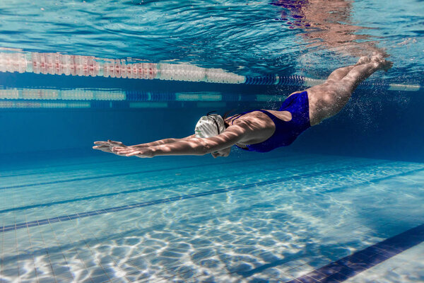 underwater picture of female swimmer in swimming suit and goggles training in swimming pool