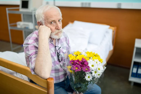 Senior man with flowers in hospital — Stock Photo