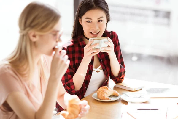 Girls eating croissants and drinking coffee — Stock Photo