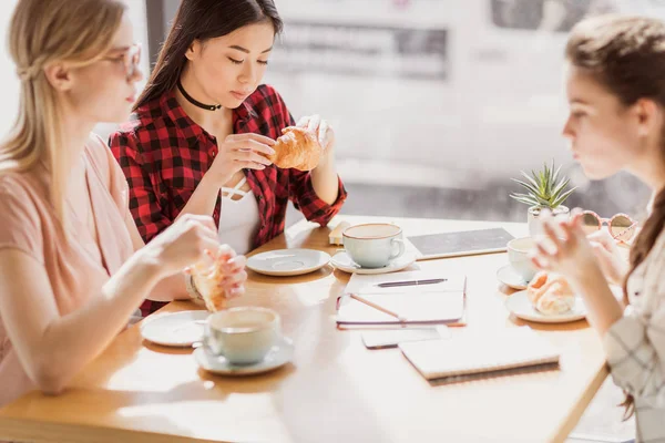 Girls eating croissants and drinking coffee — Stock Photo
