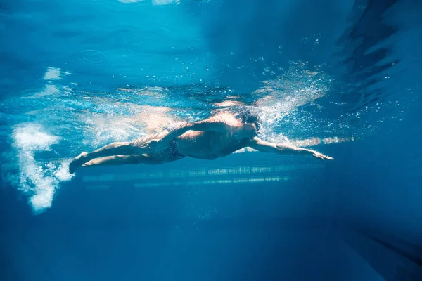 Подводная фотография молодого пловца в очках, тренирующегося в бассейне — стоковое фото