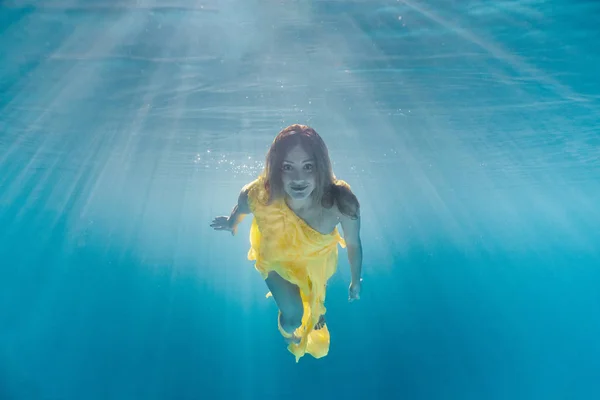 Underwater picture of beautiful young woman in dress swimming in swimming pool — Stock Photo