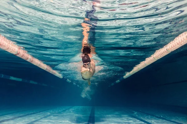 Underwater picture of young swimmer in cap and goggles training in swimming pool — Stock Photo