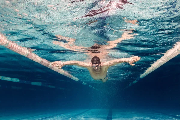 Foto subaquática do jovem nadador em boné e óculos de treino na piscina — Fotografia de Stock