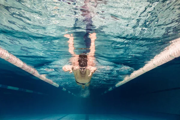 Imagen submarina de un joven nadador con gorra y gafas de entrenamiento en la piscina — Stock Photo