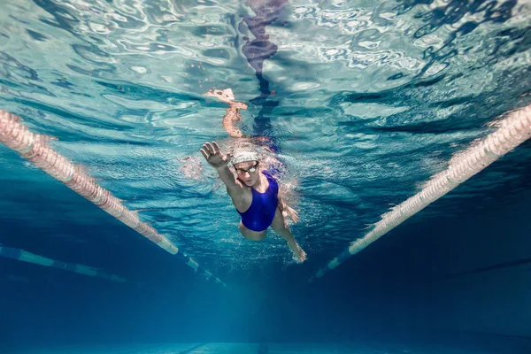 Underwater picture of female swimmer in swimming suit and goggles training in swimming pool — Stock Photo
