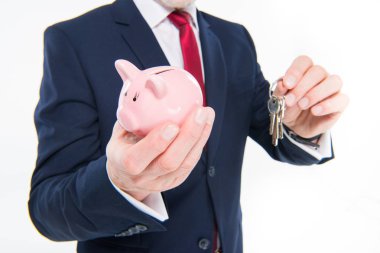 Businessman holding keys and piggy bank  clipart