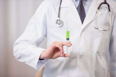 Doktor elinde şırınga tutuyor.