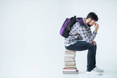 Kitap yığınının üzerinde oturan öğrenci 