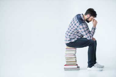 Kitap yığınının üzerinde oturan öğrenci 