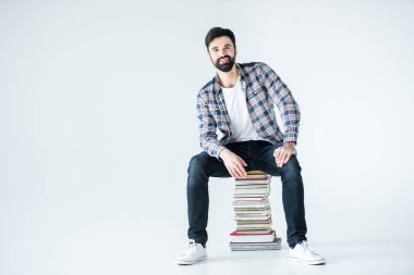 Kitap yığınının üzerinde oturan öğrenci 