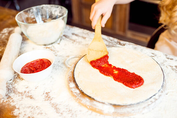 girl putting sauce on dough