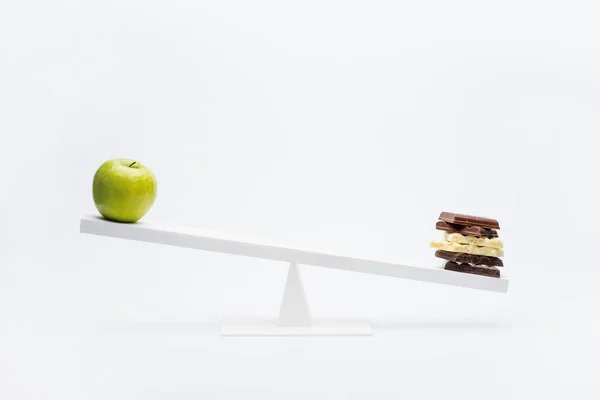 Apple and chocolate on seesaw — Stock Photo, Image