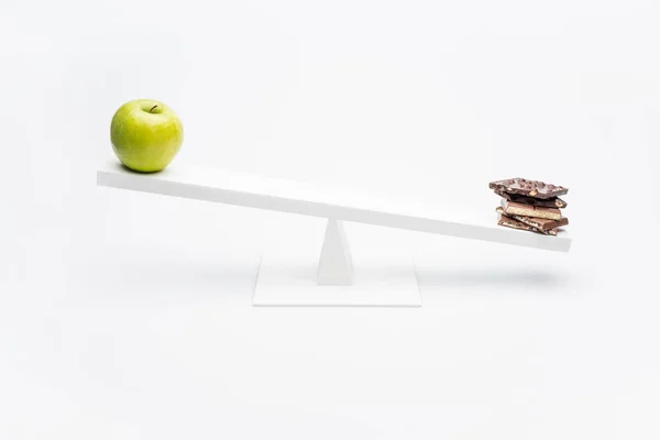 Apple and chocolate on seesaw — Stock Photo, Image