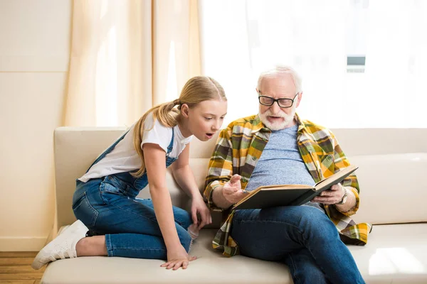 Дедушка с девушкой читает книгу — стоковое фото
