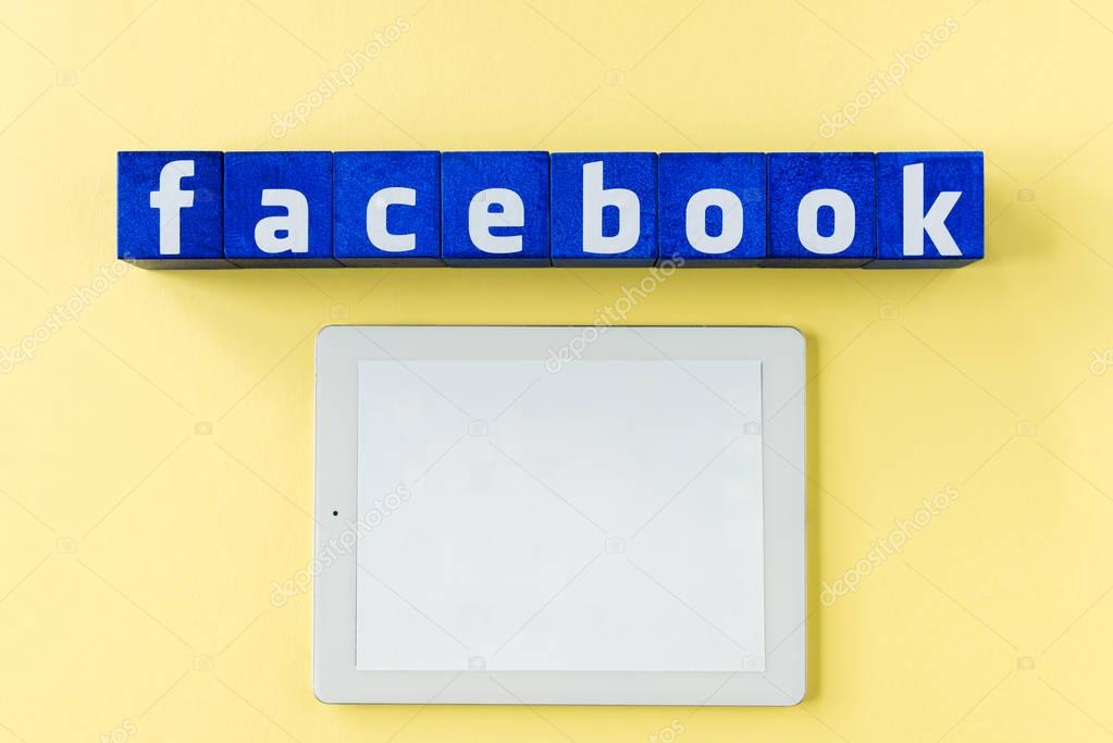 Facebook logo made from blue cubes with digital tablet and blank screen on yellow surface