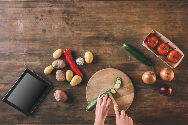 Руки режут огурец на доске для резака
 