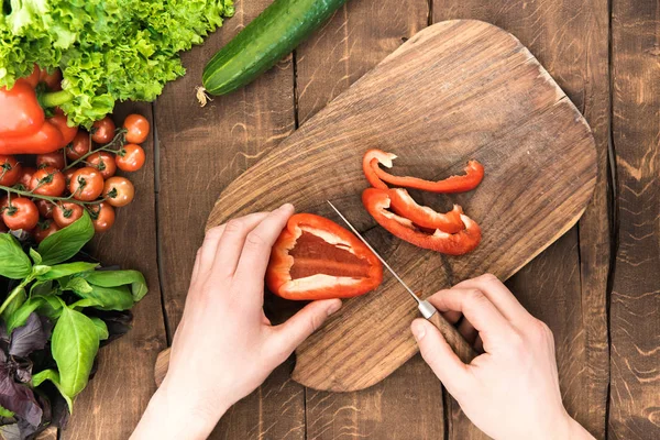 Hands cutting pepper on chopping board — Stock Photo, Image