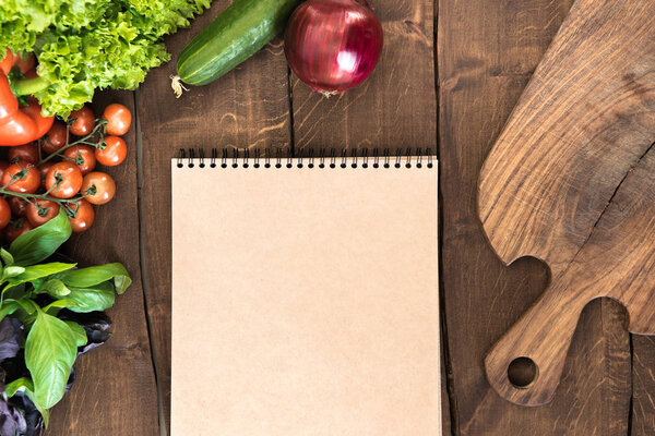 Notepad with raw vegetables on table