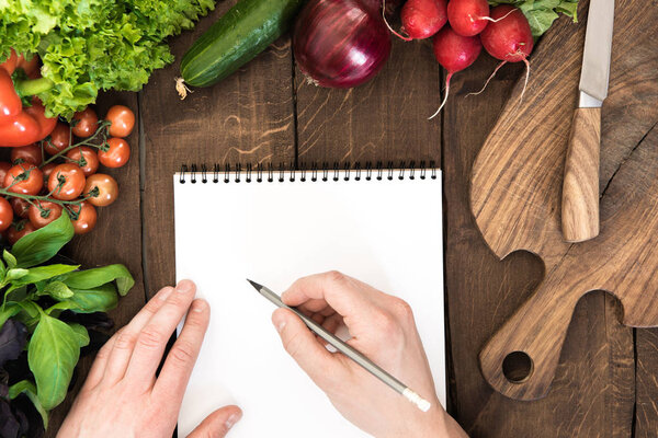 Notepad with raw vegetables on table