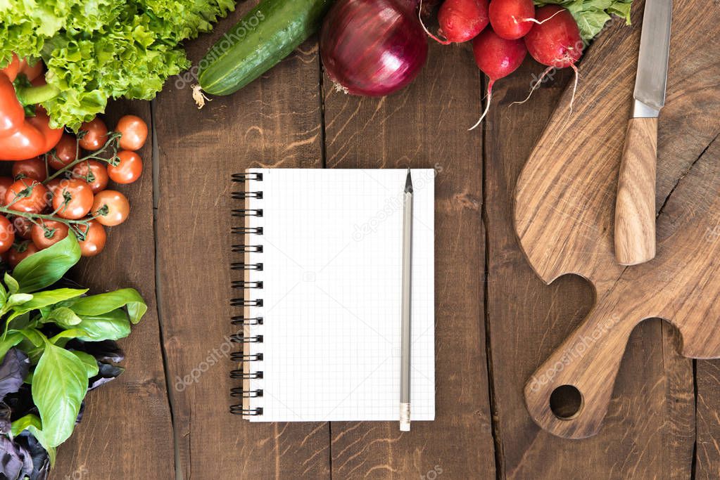 Notepad with raw vegetables on table