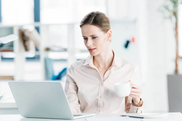 Businesswoman working on laptop and drinking coffee — Stock Photo, Image