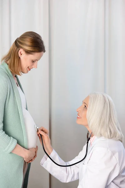 Médico escuchando vientre de la mujer embarazada —  Fotos de Stock