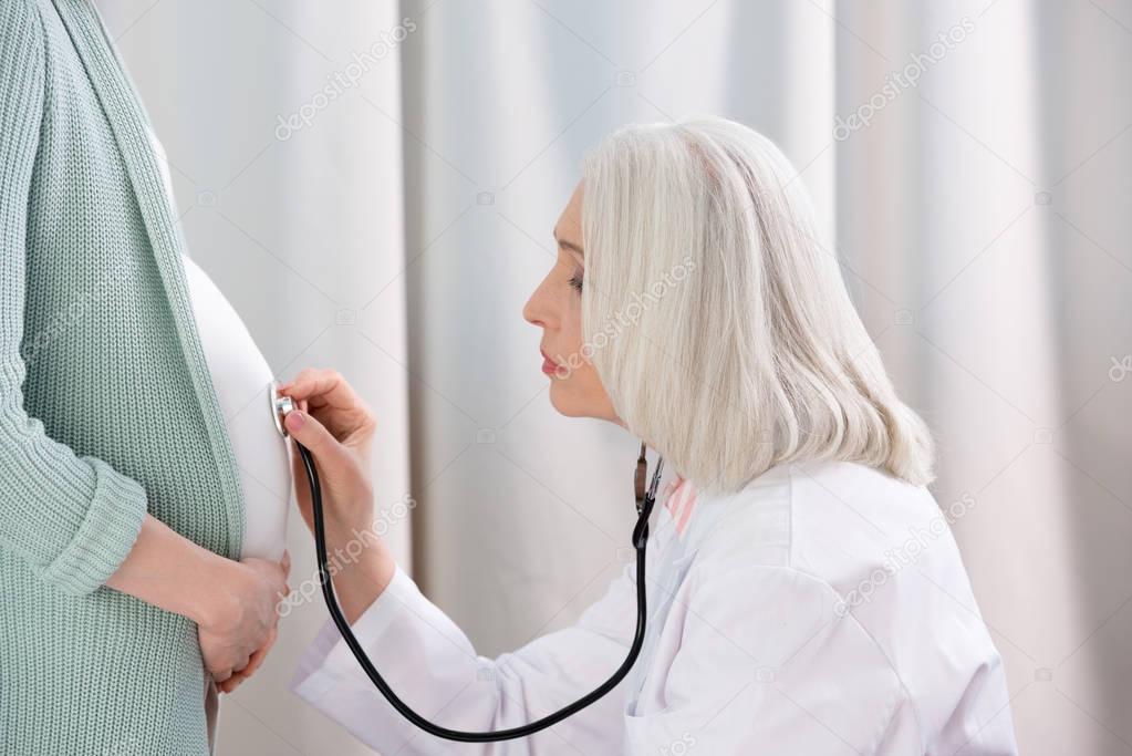 Doctor listening belly of pregnant woman 