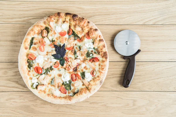 Italian pizza with cutter on wooden tabletop — Stock Photo, Image