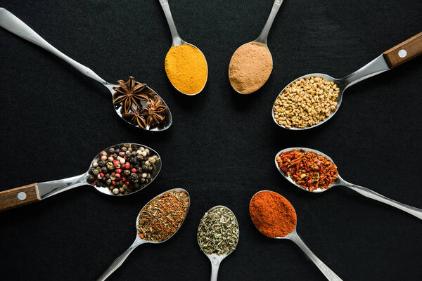 various spices and herbs in metal spoons