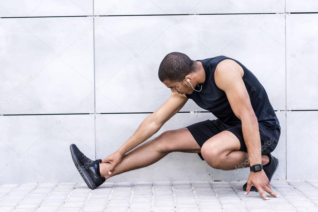 african american sportsman stretching on street