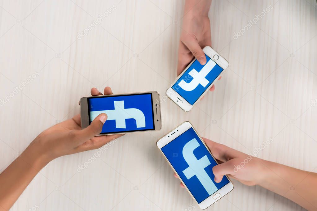 Cropped shot of teenagers holding smartphones with facebook logo on screens in hands