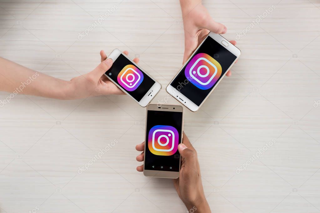 Cropped shot of teenagers holding smartphones with instagram logo on screens in hands