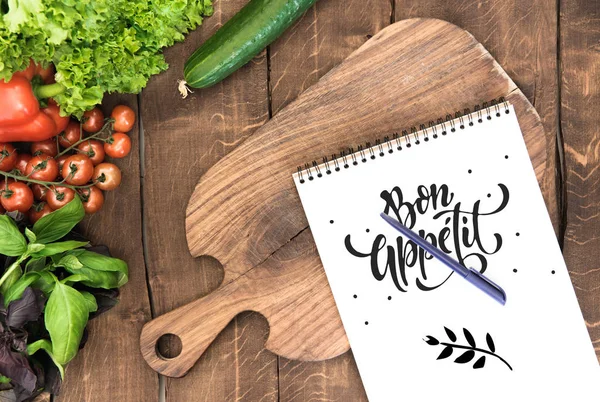 Notepad with raw vegetables on table