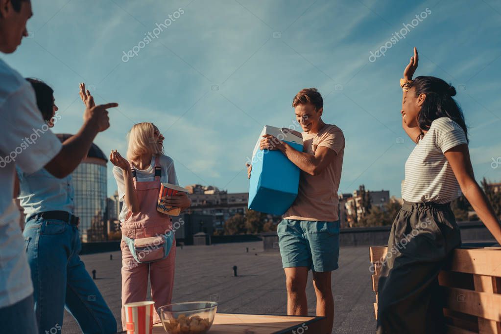 Group of happy friends with fridge container of beer on roof