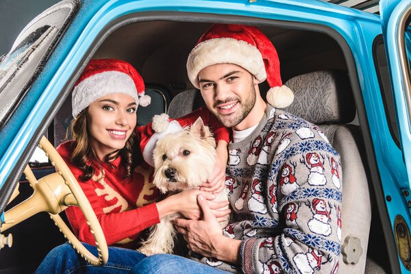 family in santa hats with dog in car