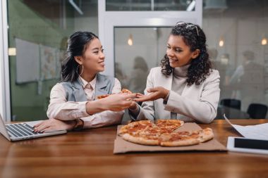pizza yiyor ve ofiste siyah ve Asya iş kadınları