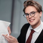 Joven hombre de negocios sonriente en anteojos trabajando con plano