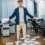 Бизнесмен в офисе с пустыми бумагами на полу вокруг него