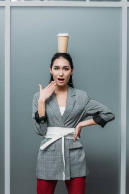 surprised asian woman with disposable cup of coffee on head clipart