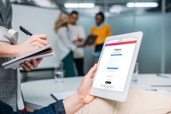 бизнесмен держит планшет с Instagram на экране в современном офисе, а коллега делает заметки
